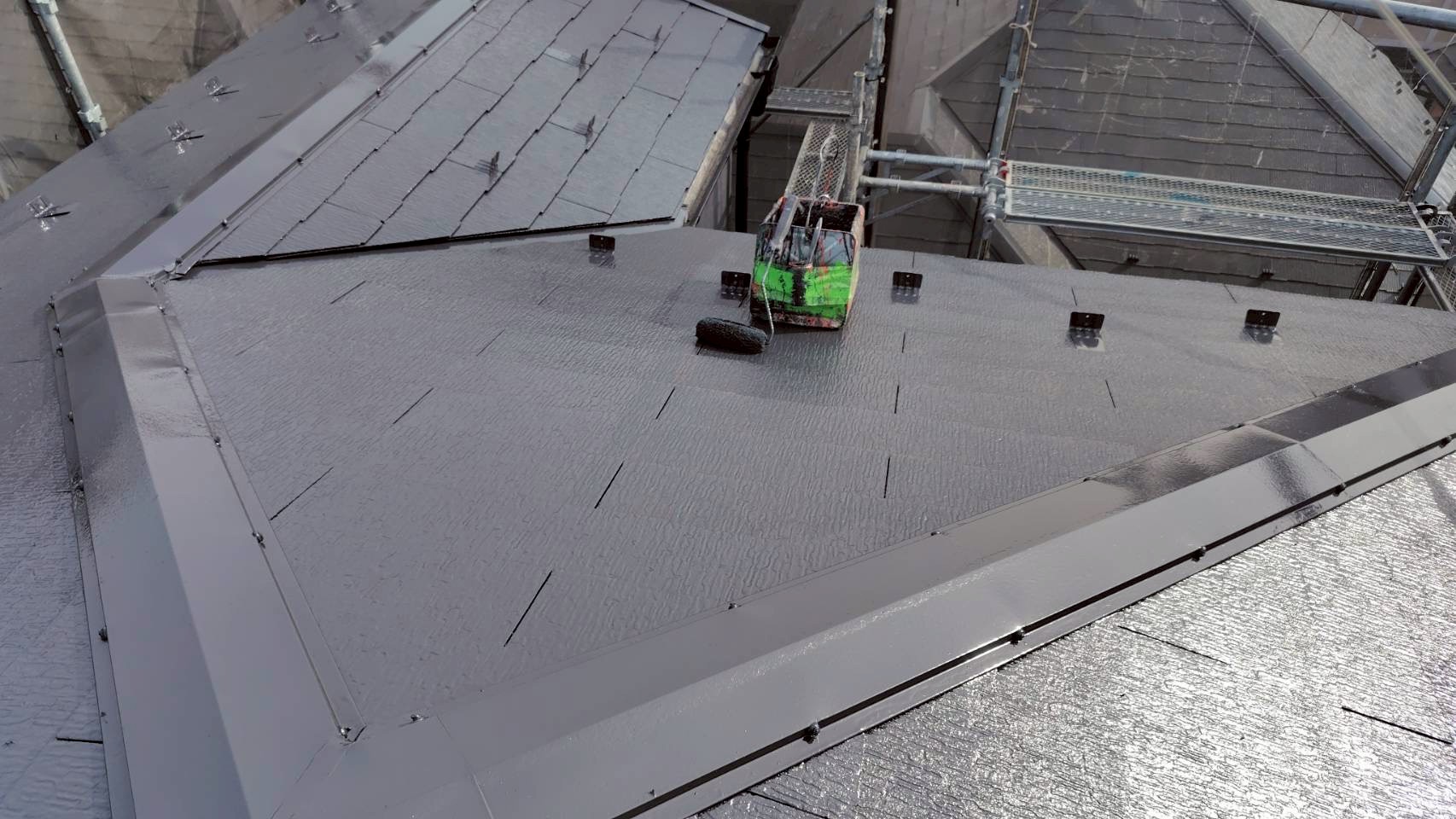 グレーの塗料で上塗り作業中のスレート屋根